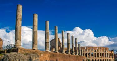 beautiful view of Colosseum with ancient columns on blue sky background with dramatic white clouds. view from Via Sacra, Rome, Italy