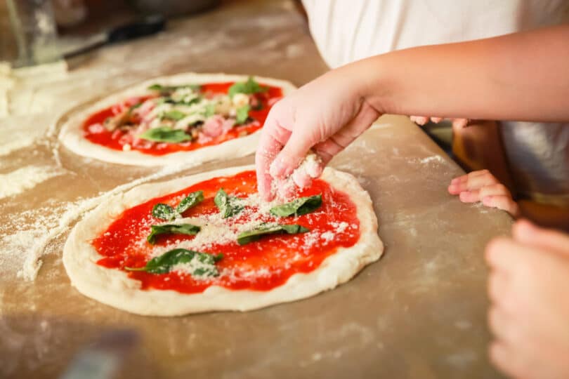 Preparing Pizza Margherita, the archetype of Neapolitan pizza. Cook adds grated parmesan cheese. Selective focus