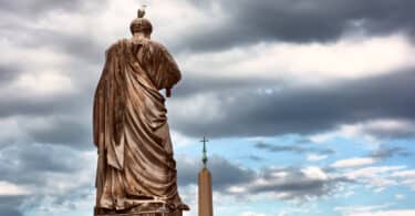 The back of the Saint Peter statue and the obelisk outside the Papal Basilica of Saint Peter