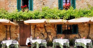 Things to do in Tuscany - Cafe tables and chairs outside a quaint stone building in Tuscany, Italy