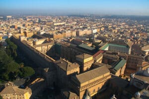 Aerial view of the Vatican Museums complex in Vatican City, showing long rectangular galleries, courtyards, and adjoining Renaissance palaces with Rome spread out beyond.