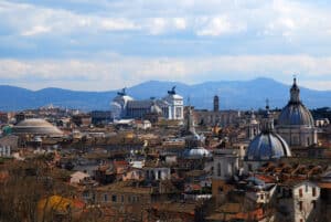 Panoramic view of Rome showing the Pantheon’s dome on the left, multiple church domes, and the white Monument to Victor Emmanuel II (Vittoriano) with winged chariots, with hills in the background.