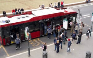 A crowded red city bus in Rome with passengers boarding at a busy stop