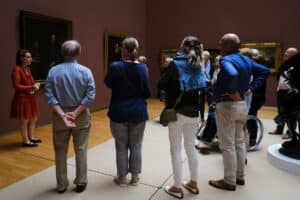 Museum guide speaking to a small group in an art gallery, pointing toward exhibits.